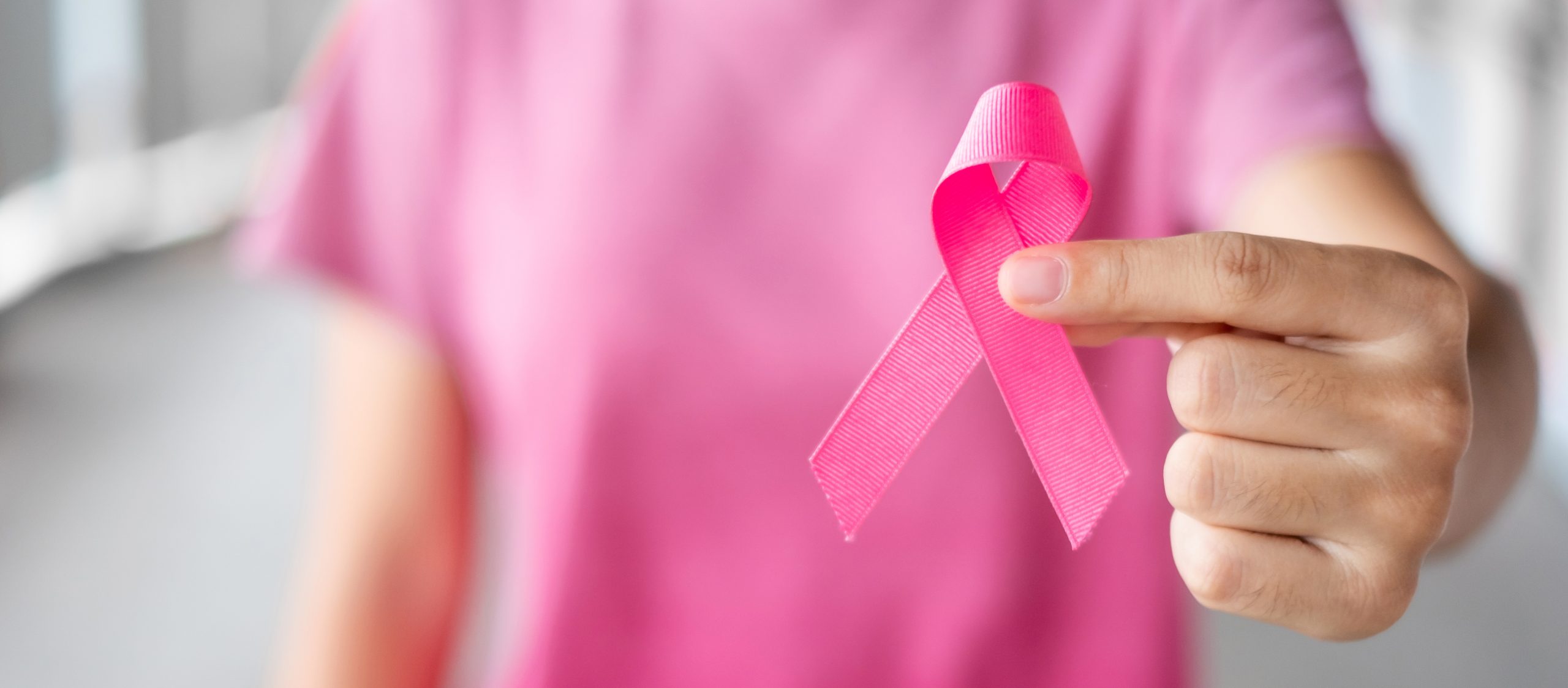 Frau mit pinkem Oberteil hält eine rosa Schleife für Brustkrebsbewusstsein